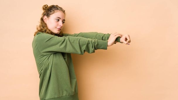 Молода біла жінка ізольована на бежевому тлі розтягування рук, розслаблене положення
. - Фото, зображення