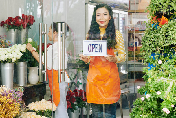 Belle jeune femme vietnamienne collant signe ouvert sur la porte en verre du magasin de fleurs - Photo, image