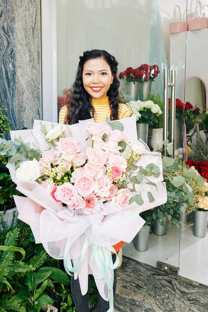 幸せな若いベトナムの花屋を示す大きな美しい花束の肖像彼女は顧客のために作った - 写真・画像