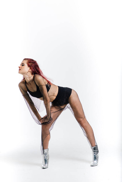Jovem bela fêmea flexível em um macacão preto e salto alto está posando em um estúdio de dança. - Foto, Imagem