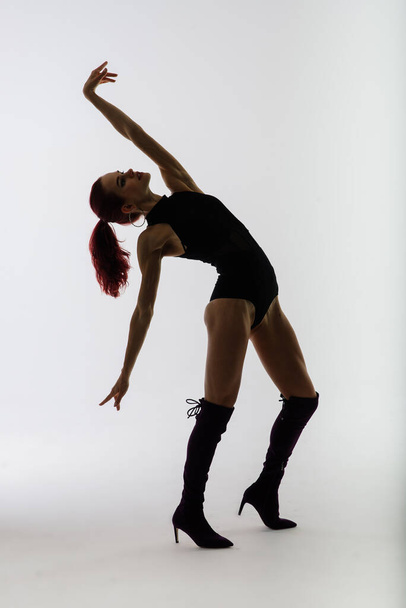 Młoda, piękna, elastyczna kobieta w czarnym kombinezonie i wysokich obcasach pozuje w studio tańca. - Zdjęcie, obraz