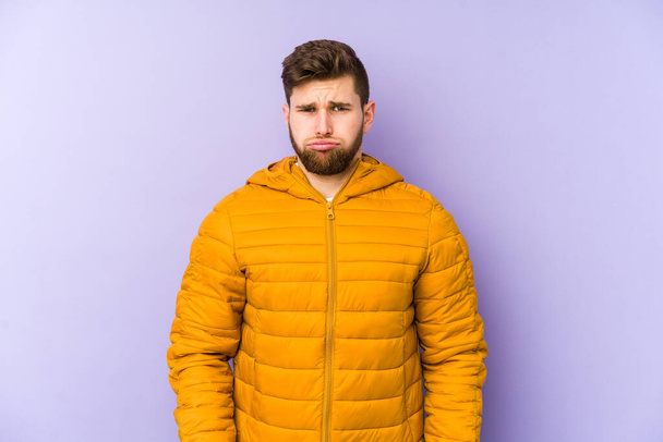 Young man isolated on purple background blows cheeks, has tired expression. Facial expression concept. - Photo, Image
