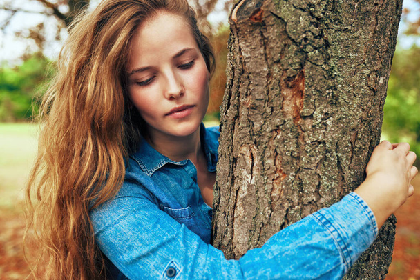 Pretty young woman wearing a blue denim shirt hugging a big tree in the park posing on nature background.  - Foto, Imagem