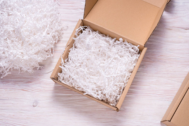Shredded paper filler in cardboard box on wooden table  - Фото, изображение