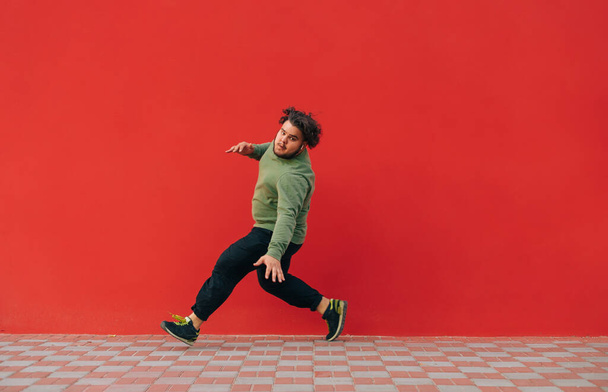 Fat dancer shows hip hop performance on red wall background. Overweight man dancing breakdance on red background - Photo, image