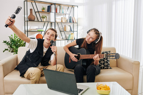 Yetenekli yaratıcı genç çift şarkı söyleyip gitar çalarken kendilerini filme alıyorlar. - Fotoğraf, Görsel