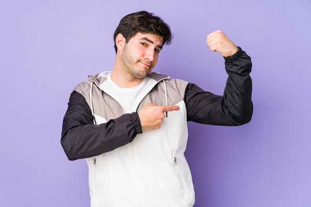 Mladý muž izolovaný na purpurovém pozadí ukazující sílu gesto s pažemi, symbol ženské moci - Fotografie, Obrázek