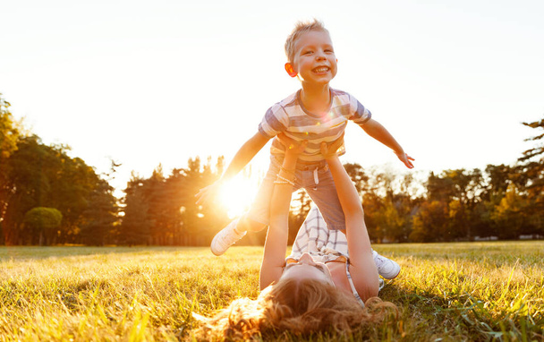 Happy family: mother   lying on   grass and throwing up cheerful little son in nature in summe - Foto, Imagem