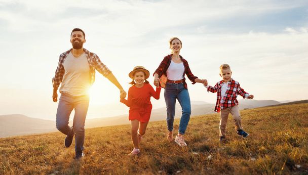 Glückliche Familie: Mutter, Vater, Kinder Sohn und Tochter laufen bei Sonnenuntergang in der Natur - Foto, Bild