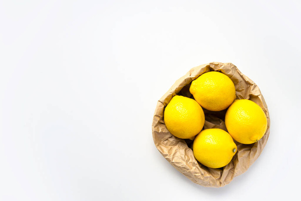 White background and eco packing with lemon. Four ripe lemon on grey background. Group of fresh lemon in recycling paper bag. Place for text, copy space - Foto, Imagen