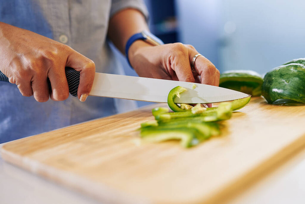 Крупный план, как домохозяйка режет зеленый перец при приготовлении салата на ужин - Фото, изображение