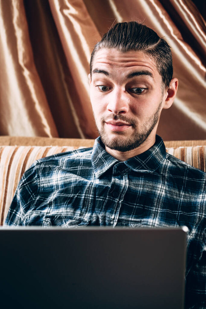 Um belo jovem freelancer de camisa azul trabalha em um laptop prateado em casa. Trabalho remoto durante a quarentena. - Foto, Imagem