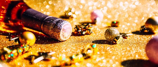 Christmas or New Year composition with bottle of rose champagne and golden sparkling decoration on golden shiny background, side view with festive bokeh and shadows. Party Celebration creative concept - 写真・画像