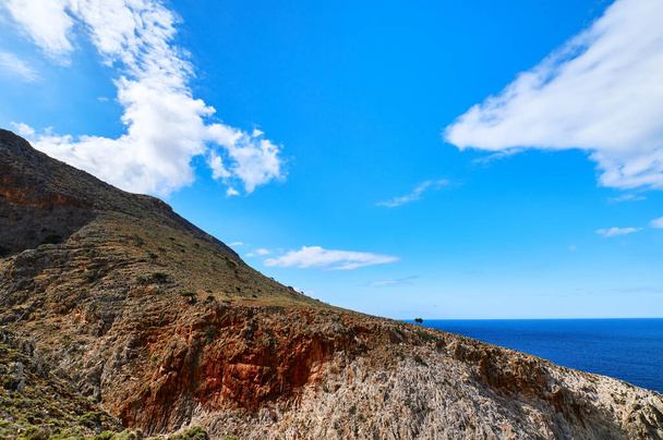 Beautiful wild red cliffs, clear blue sky, clouds. Diagonal view. Typical Greek landscape. Akrotiri peninsula, Chania region, Crete island, Greece - Fotó, kép