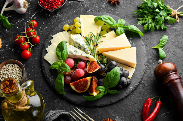 Assorted cheeses on a plate. Parmesan cheese, blue cheese and brie on a plate with grapes and figs. Antipasto. Top view. - Foto, afbeelding