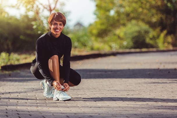 gyönyörű sportos fiatal nő összekötő cipőfűzők futás közben a parkban - Fotó, kép