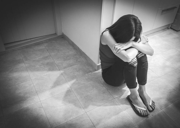 Genç beyaz kadın mutfak zemininde oturuyor ve yüzünü ellerle örtüyor. Endişe ve depresyon kavramı. Siyah ve beyaz arkaplan resmi. - Fotoğraf, Görsel
