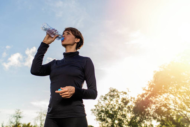gyönyörű sportos fiatal nő ivóvíz palack a parkban. kiváló minőségű fénykép - Fotó, kép