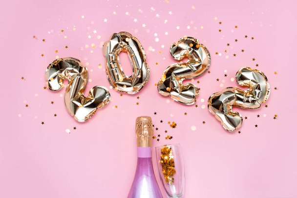 2022 gouden folie ballonnen nummers, champagne, sterren confetti, linten en bokeh. Top horizontale weergave kopieerruimte Nieuwjaar en vakantie concept. - Foto, afbeelding