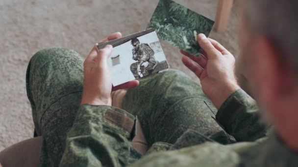 Katonai egyenruhás katona vagy tiszt válllövése fölött ül a kanapén, és képeket mutat a családjának, miközben történeteket mesél. - Felvétel, videó