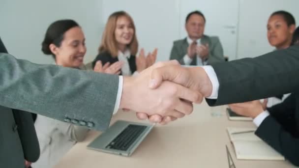 Dos irreconocibles hombres de negocios de pie uno frente al otro haciendo apretón de manos después de llegar a un acuerdo, sus compañeros de trabajo animando - Metraje, vídeo