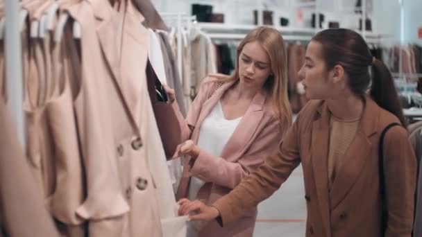 Μέτριο πλάνο χαρούμενων νεαρών γυναικών φίλων να κουβεντιάζουν και να ψωνίζουν ρούχα στο κατάστημα - Πλάνα, βίντεο