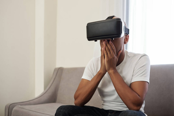 Шокированный эмоциональный молодой чернокожий мужчина играет в видеоигры или смотрит видео в очках - Фото, изображение