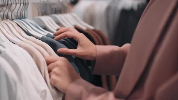 Κοντινό πλάνο με τη μέση του τμήματος αγνώριστη νεαρή γυναίκα στο σακάκι κοιτάζοντας μέσα από ράφι ρούχα - Πλάνα, βίντεο