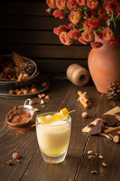 Refreshing delicious melon smoothie with cinnamon, hazelnuts and chocolate, vase of chrysanthemums and glasses of smoothie on wooden background - Photo, Image