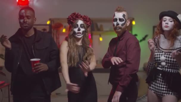 Slowmo-Aufnahme von glücklichen jungen Männern und Frauen in Halloween-Kostümen, die gemeinsam auf einer Hausparty tanzen und in die Kamera schauen - Filmmaterial, Video