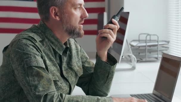 Slowmo inclinar-se de meia-idade oficial do exército masculino dos EUA em uniforme militar sentado na mesa e falando sobre walkie-talkie - Filmagem, Vídeo