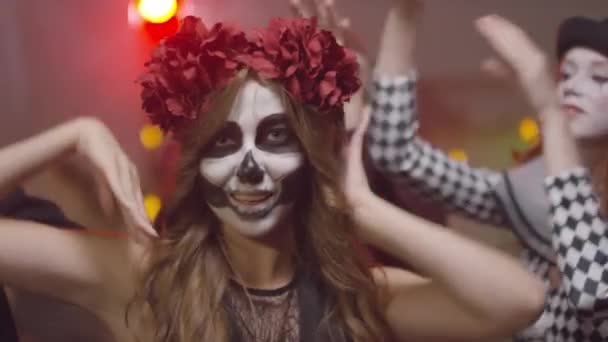 Portraitaufnahme einer jungen Frau im Halloween-Kostüm, die in die Kamera blickt und mit ihren Freunden auf einer Hausparty tanzt - Filmmaterial, Video
