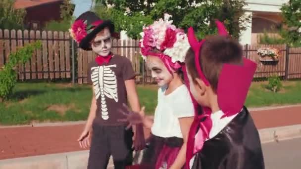 Tracking shot de niños en disfraces de Halloween llevando cestas y caminando en el barrio suburbano - Metraje, vídeo