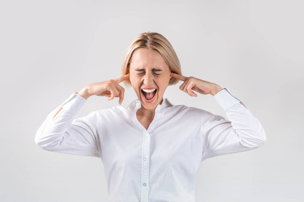 Attraktive Geschäftsfrau schließt die Ohren und schreit vor Wut auf hellgrauem Studiohintergrund - Foto, Bild