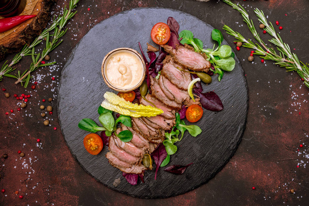 Sliced roast beef with leaves of salad on dark plate  - Foto, immagini