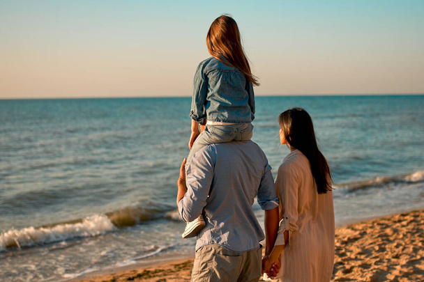 Glückliches Familienkonzept. Junge attraktive Mutter, gutaussehender Vater und ihre kleine süße Tochter spazieren zusammen am Strand. - Foto, Bild