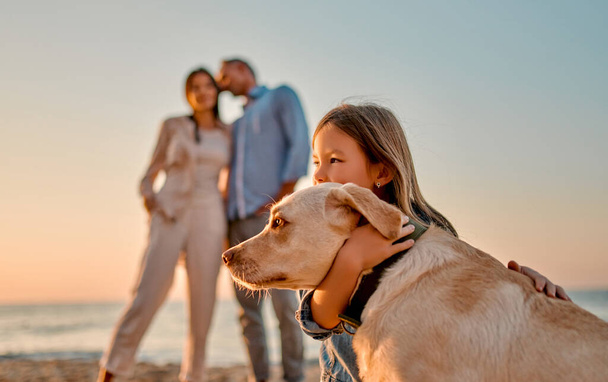 Happy family concept. Young attractive mother, handsome father and their little cute daughter standing together on the beach with dog. - Foto, Bild