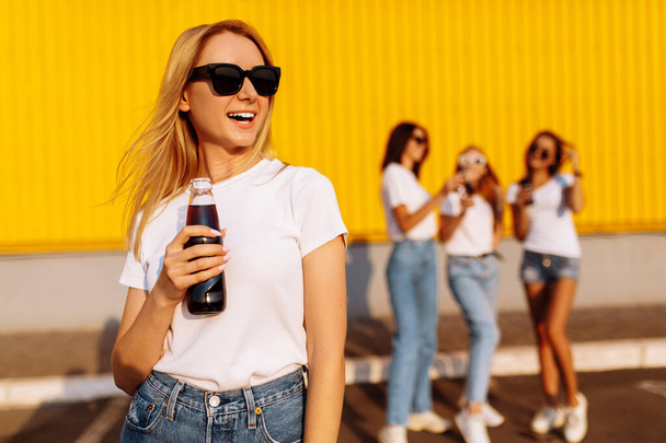 happy young woman in sunglasses drinks a drink on a sunny summer day, in the background with girlfriends near the mall - Fotoğraf, Görsel