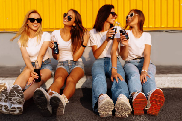 Young happy friends drinking a drink and having fun together on a sunny summer day against the background of a yellow wall, concept of friendship and celebration - Fotoğraf, Görsel