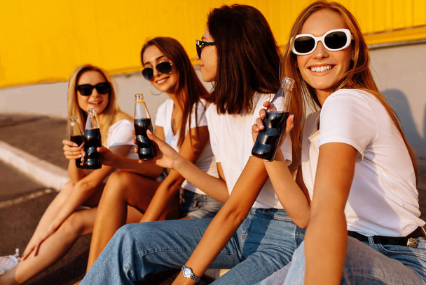 happy friends drinking a drink and having fun together on a sunny summer day against the background of a yellow wall of a shopping mall, concept of friendship and celebration - Foto, Imagen