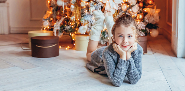 Pieni tyttö lahjapakkaus lähellä joulukuusi jouluaattona kotona. Nuori poika kevyessä makuuhuoneessa talven koristelu. Joulun uudenvuoden joulukuun aika juhlan konseptille. Banneri - Valokuva, kuva
