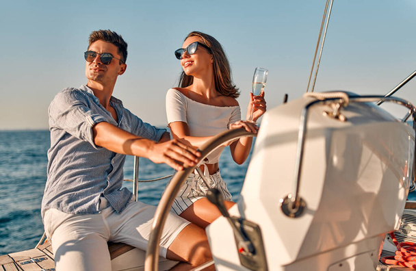 Group of friends relaxing on luxury yacht. Having fun together while sailing in the sea. Romantic couple sitting near steering wheel. Traveling and yachting concept. - Photo, Image