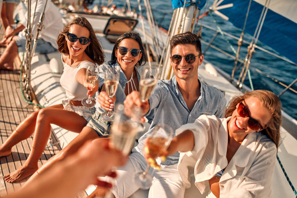 Cheers! Group of friends relaxing on luxury yacht and drinking champagne. Having fun together while sailing in the sea. Traveling and yachting concept. - Foto, afbeelding