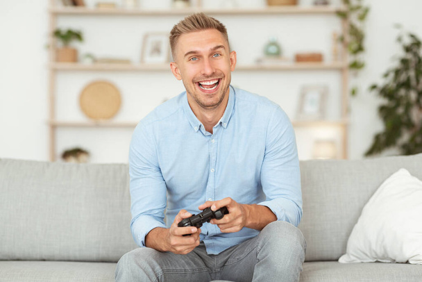 Opgewonden emotionele man zittend op de bank videospelletjes spelen - Foto, afbeelding