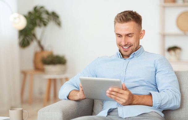Glücklicher Kerl mit digitalem Tablet sitzt auf der Couch - Foto, Bild
