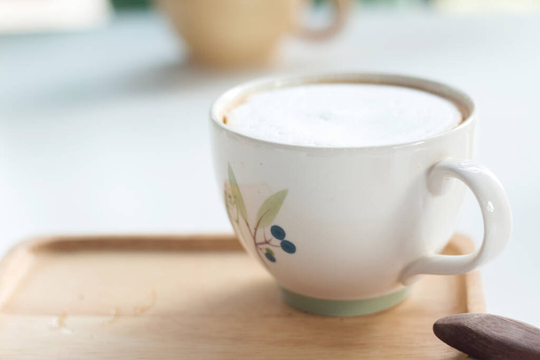 Κλείστε ένα φλιτζάνι ζεστό καφέ latte σε λευκό τραπέζι. - Φωτογραφία, εικόνα
