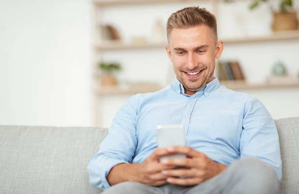 Szoros kép mosolygós fickó használ okostelefon az otthonában - Fotó, kép