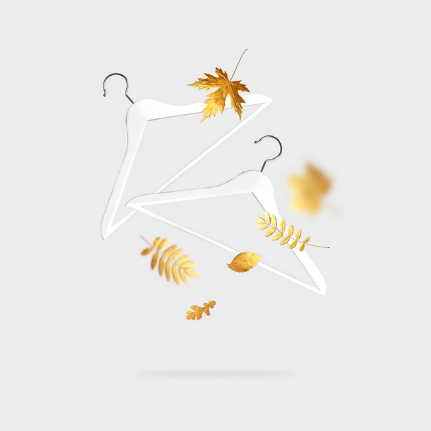Fliegende weiße hölzerne Kleiderbügel, herbstlich goldene Blätter auf grauem Hintergrund. Kreative Mode, Kleidungsaufbewahrungsaccessoires. Mode, Stil, Herbstschlussverkauf und Rabatte in den Geschäften - Foto, Bild