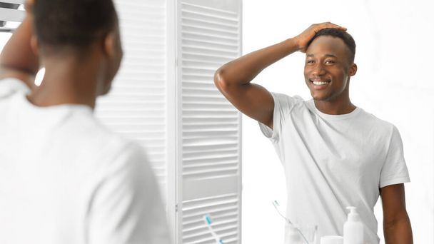 Komea Afrikkalainen mies koskettaa hiuksia seisoo lähellä peiliä kylpyhuoneessa - Valokuva, kuva