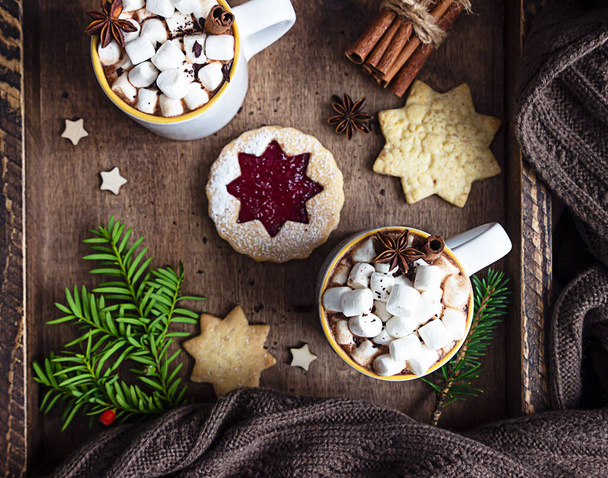 Wooden tray with ceramic cups of hot chocolate or cocoa with marshmallow, cinnamon and anise, shortcrust cookies and pieces of bitter chocolate. Winter time, holiday concept. Selective focus. - Photo, image